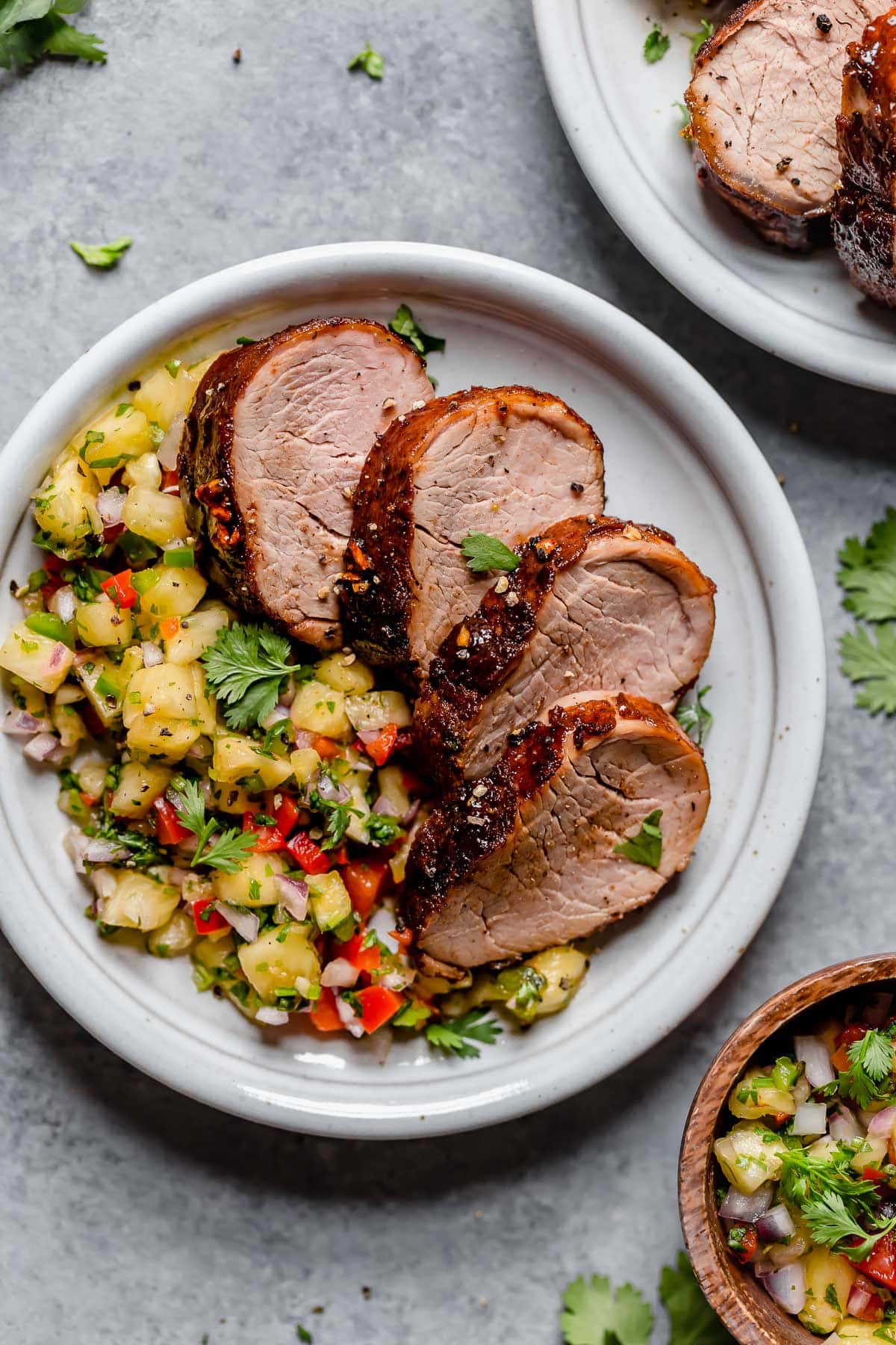 Island Pork Tenderloin Pork tenderloin cut into slices on a serving plate with a side of pineapple salsa.