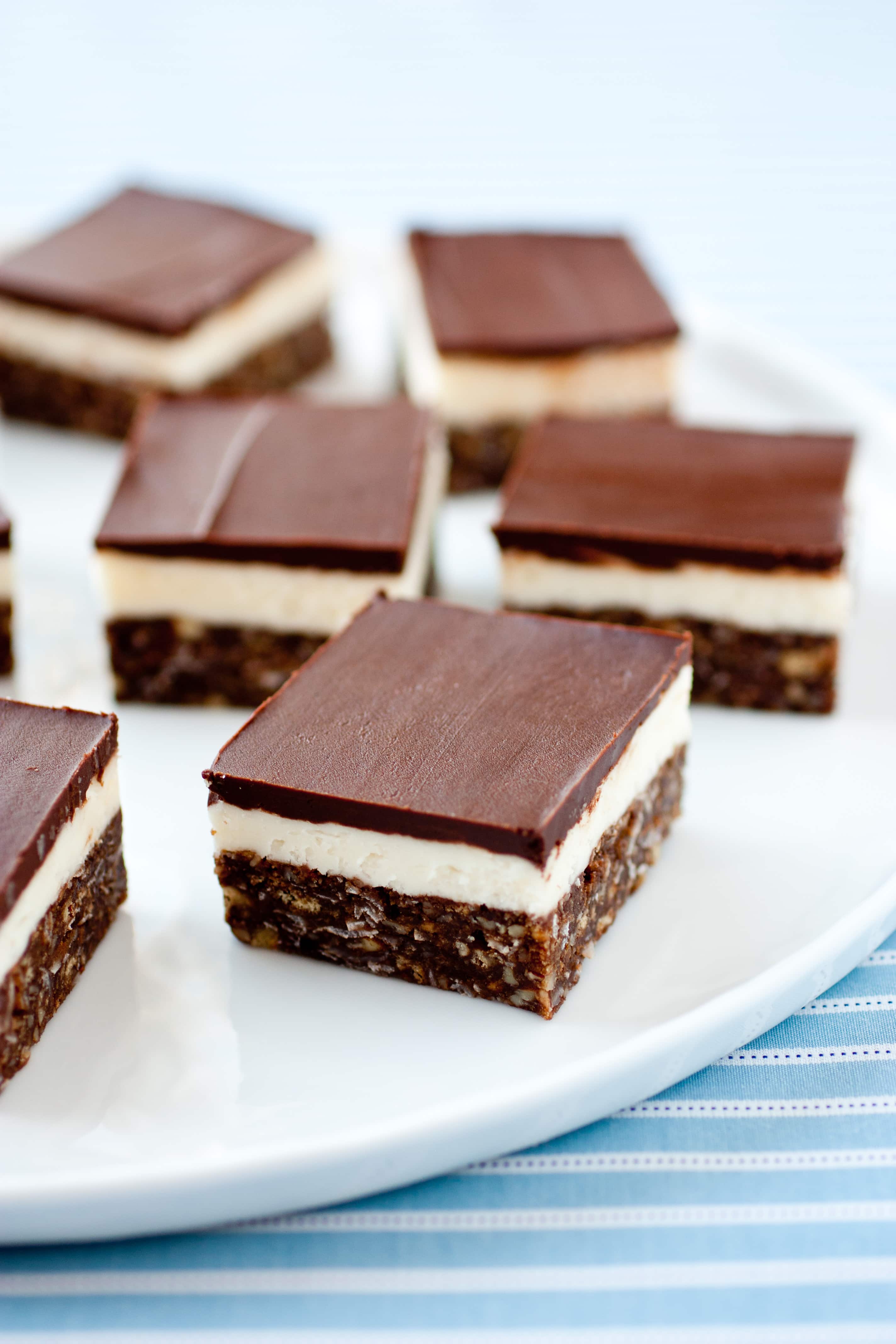 Nanaimo Bars Nanaimo Bars shown on a white serving platter set over a blue striped cloth.