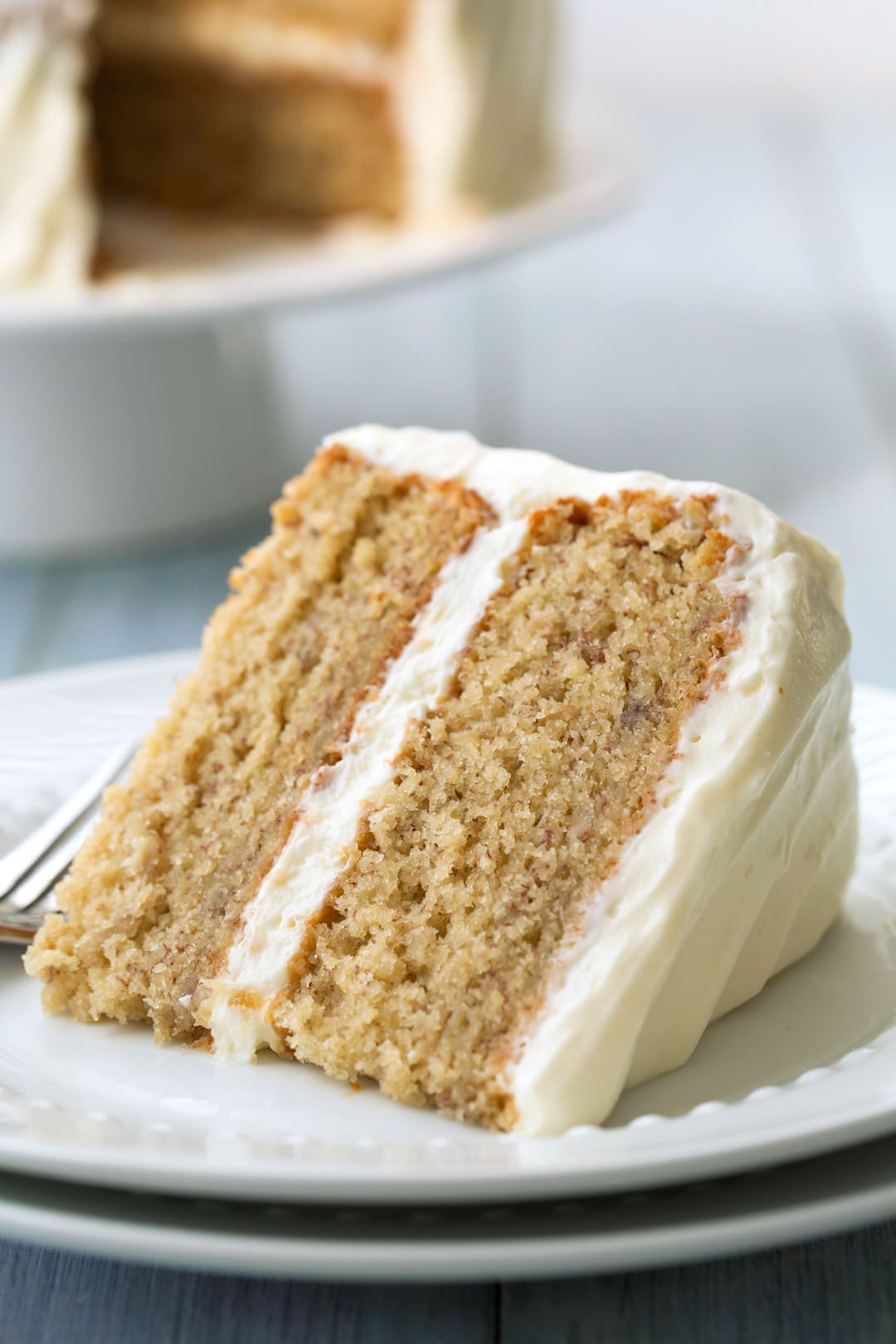 slice of Banana Cake with cream cheese frosting on a white plate