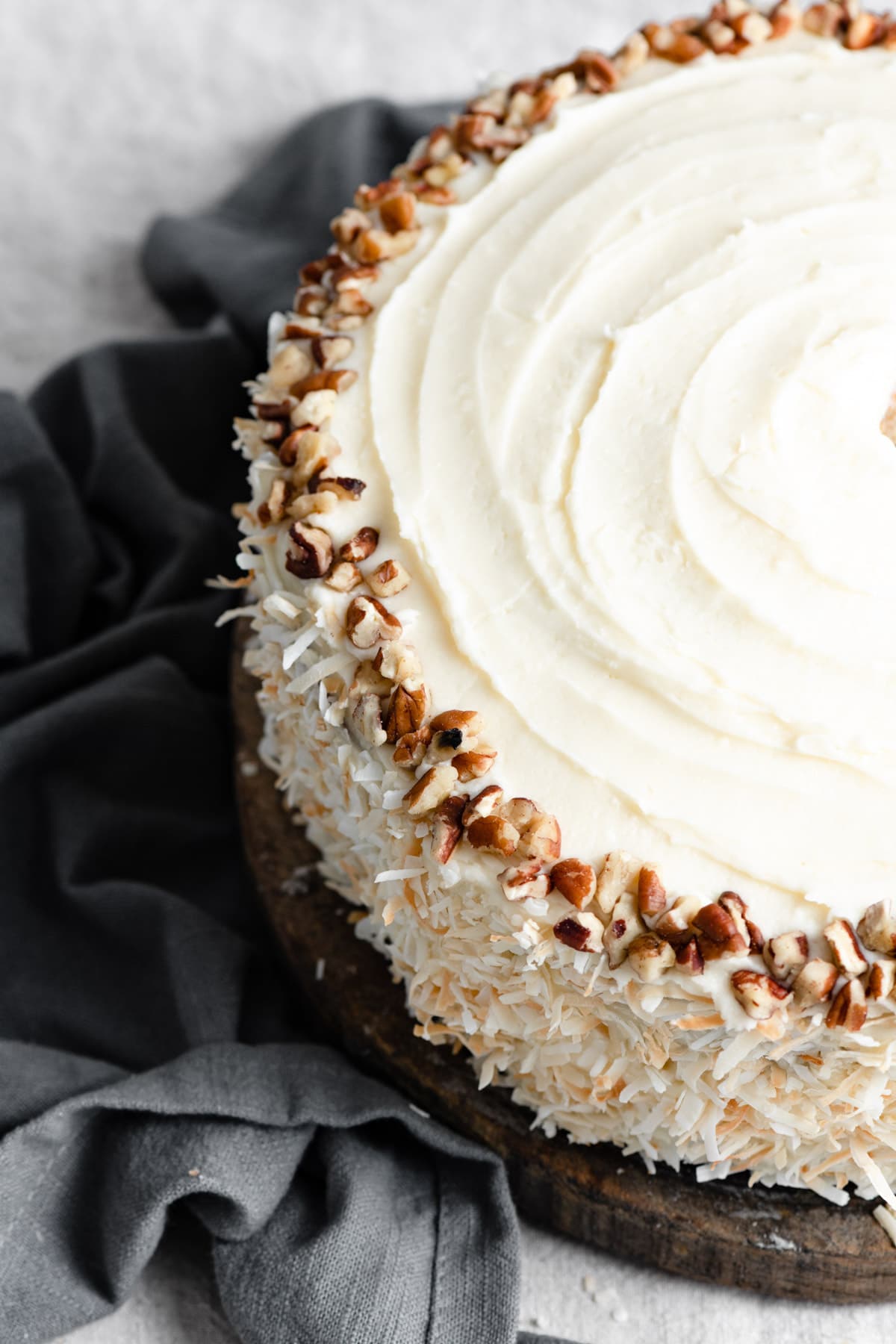 Hummingbird Cake Close up image of whole hummingbird cake showing cream cheese frosting, coconut decorated edges and a ring of pecans on top.