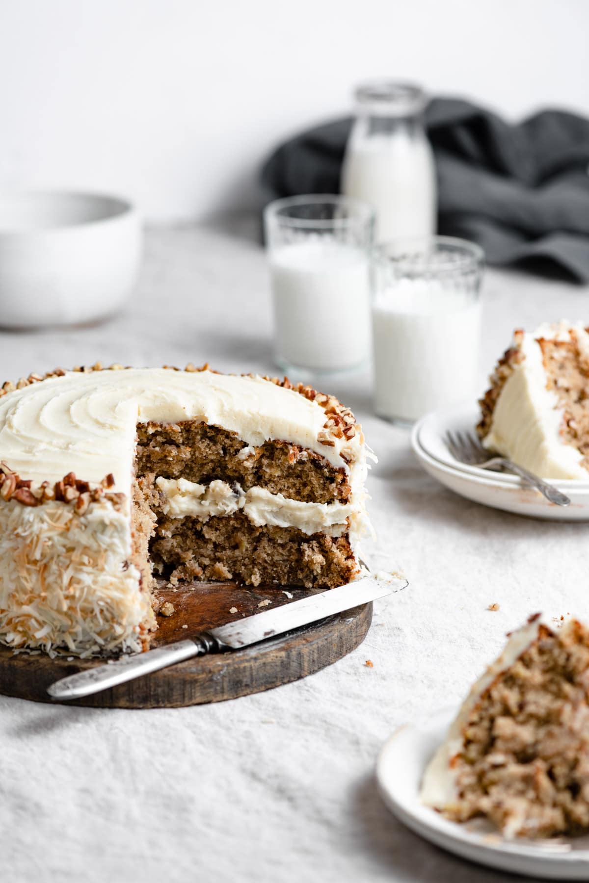 Hummingbird Cake Hummingbird cake shown with a quarter of the cake removed, cake is sitting on a wooden platter. Slices of cake are shown of the the right side.