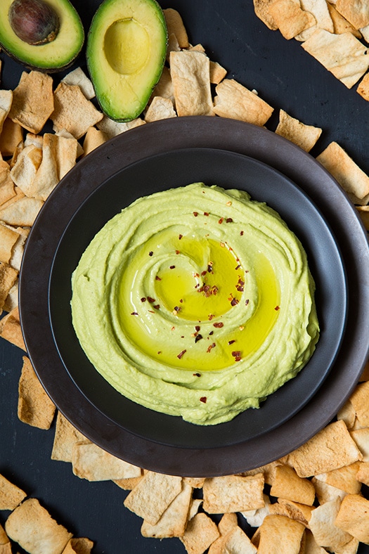 This creamy delicious homemade hummus recipe is the best! It can be made in under 10 minutes and it makes the perfect midday snack for you and your family, or take it to a party and impress your friends! #cookingclassy #hummus #avocado #dips Avocado hummus in a bowl with sliced avocado at the side