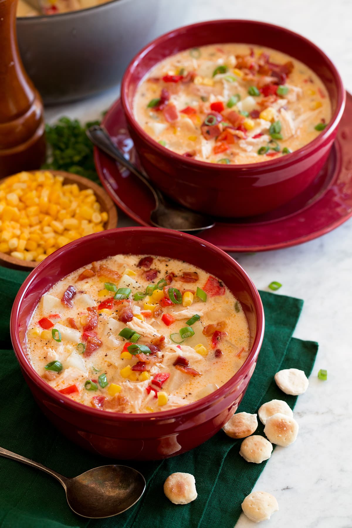 Creamy Chicken Corn Chowder Two servings of chicken corn chowder in red bowls sitting over a green cloth on a marble surface.