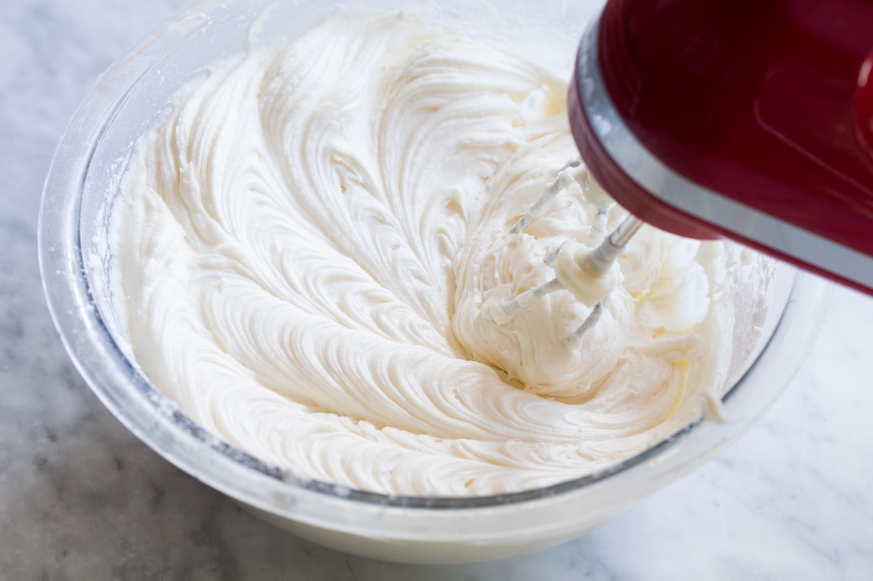 The BEST Red Velvet Cake! Soft, moist and perfectly fluffy! Mixing cream cheese frosting in glass mixing bowl with an electric hand mixer.