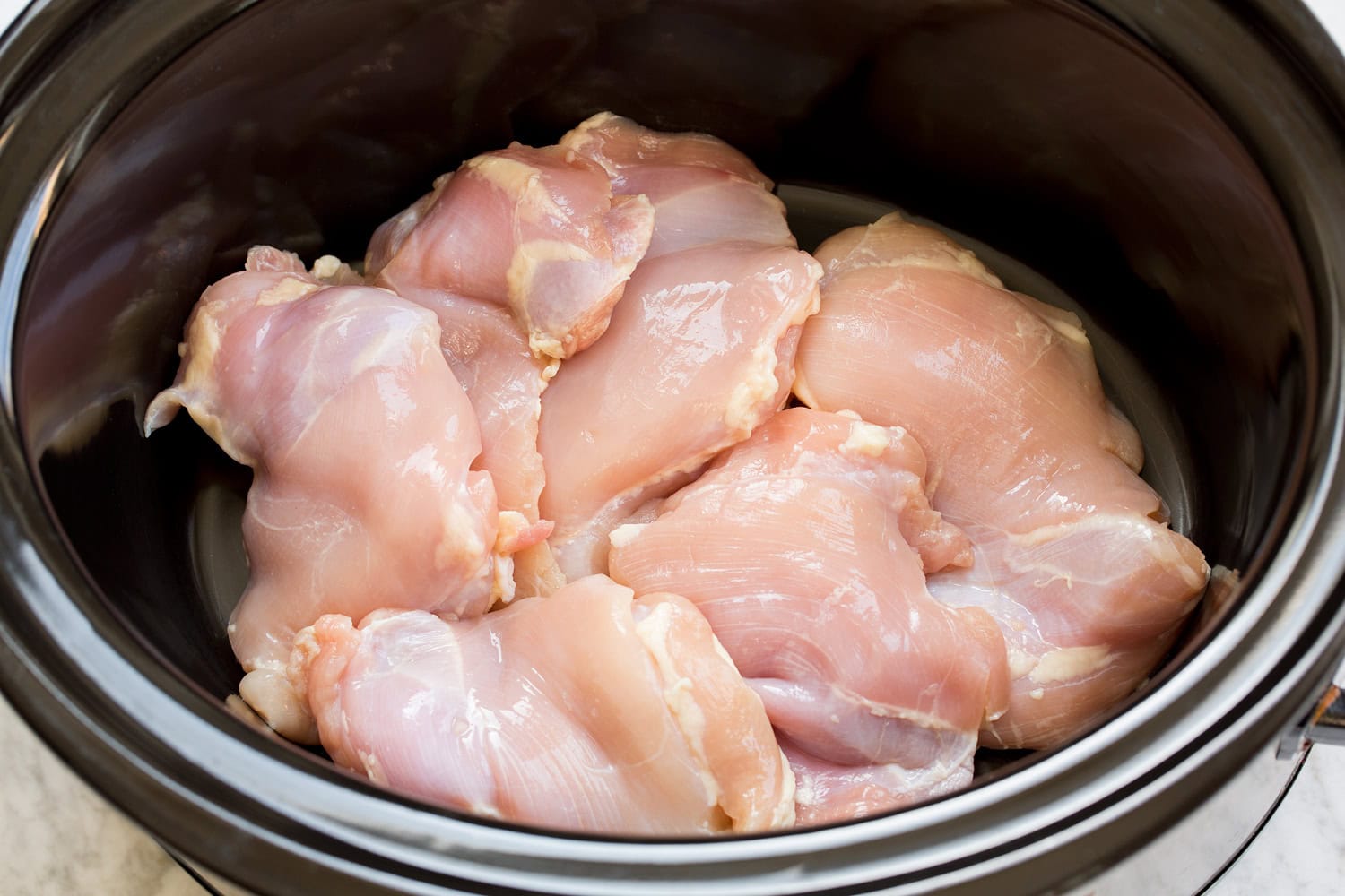 Slow Cooker Chicken Tortilla Soup Raw chicken thighs in a crockpot insert.