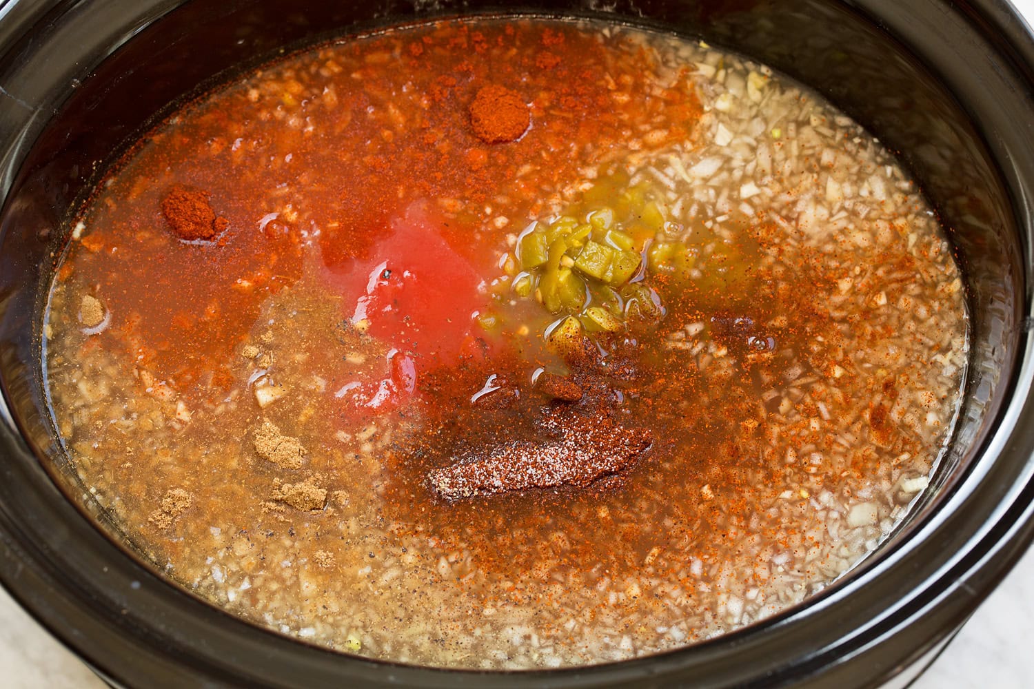 Slow Cooker Chicken Tortilla Soup Broth, onions, seasonings, green chilies over chicken layer in slow cooker.