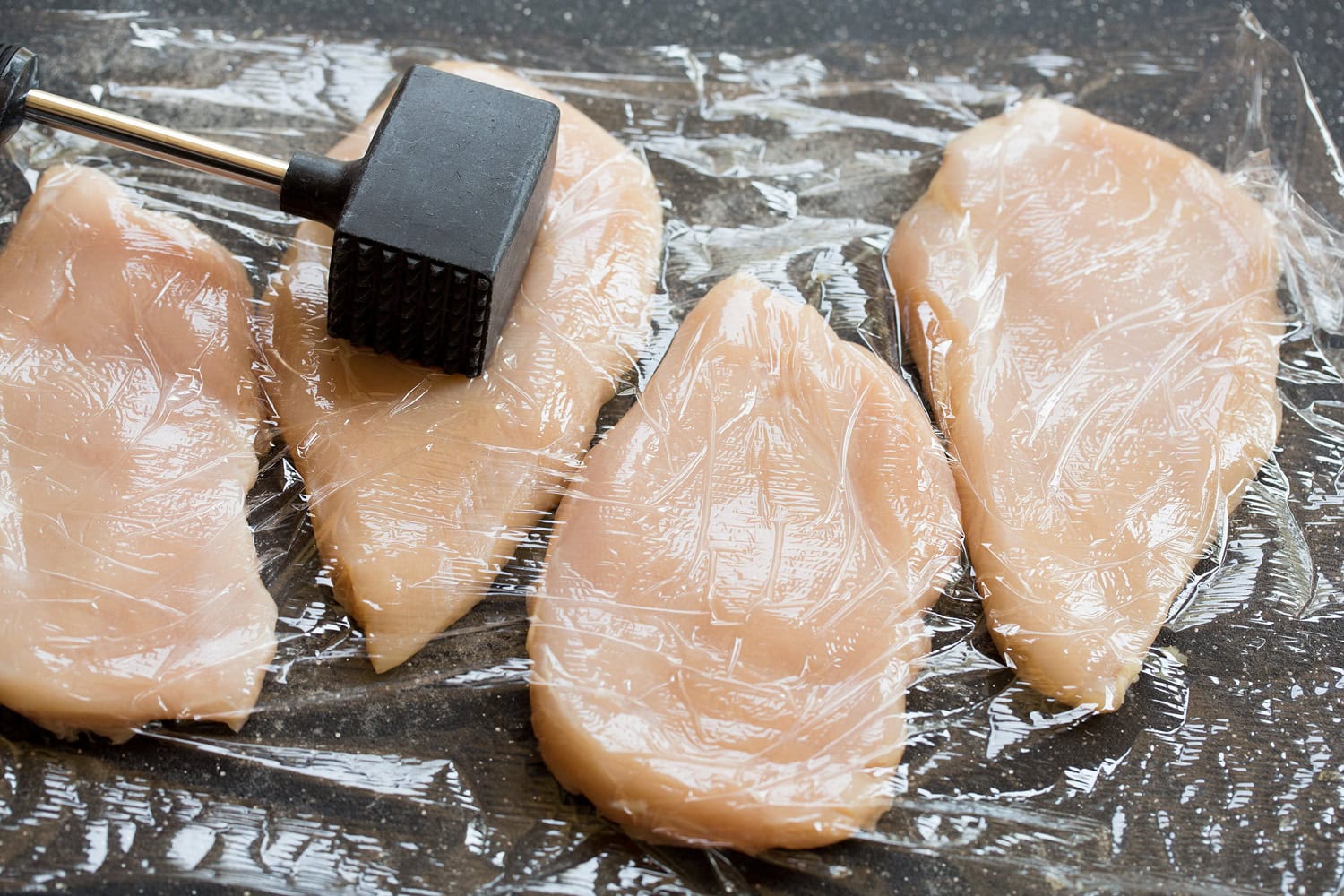 Creamy Dijon Mustard Chicken Flattening chicken breasts with a meat mallet on a cutting board.