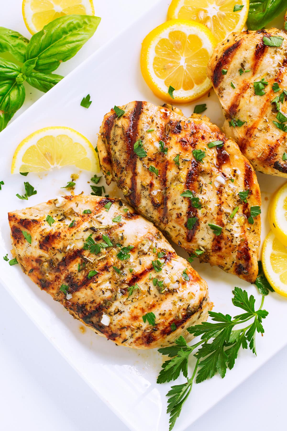 Greek Lemon Chicken Close up image of grilled chicken breasts with herb topping and char marks.