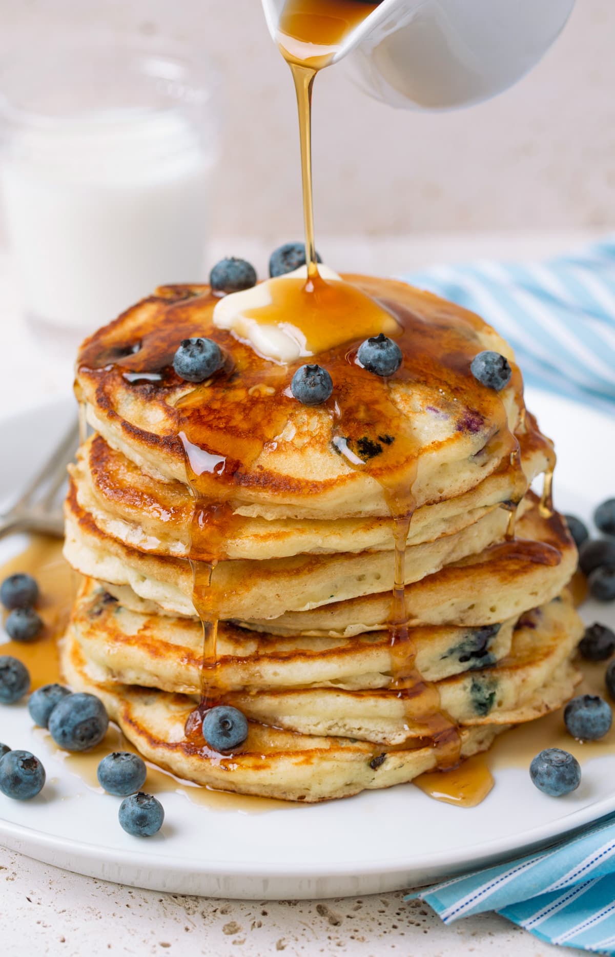 Blueberry Pancakes Pouring syrup over stack of homemade blueberry pancakes