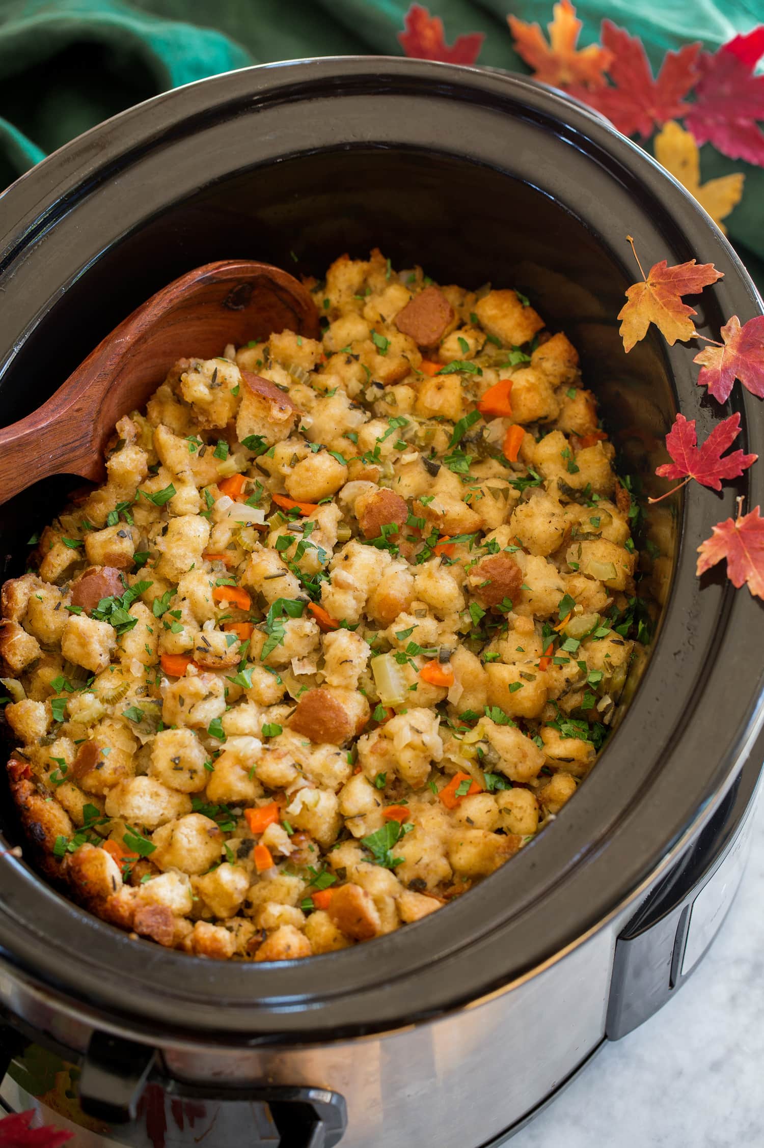 Crockpot Stuffing Stuffing in a crockpot with decorative fall leaves and a green cloth to the side.