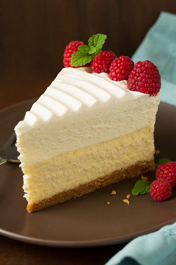 Vanilla Bean Cheesecake Slice of cheesecake on a brown serving plate, garnished with whipped cream and berries.
