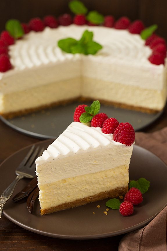 Vanilla Bean Cheesecake Slice of cheesecake on a plate with a whole cheesecake in the background.