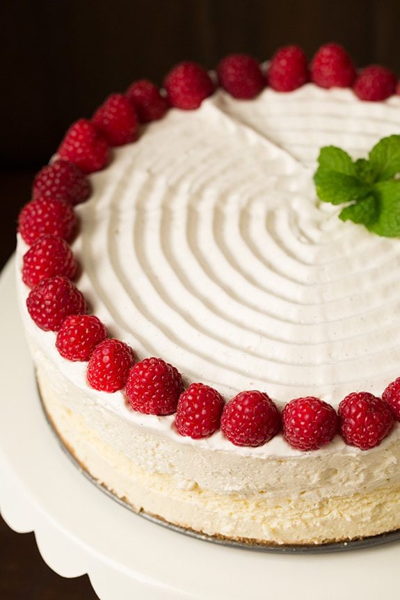 Vanilla Bean Cheesecake Image of a whole cheesecake decorated with swirled whipped cream on top, fresh raspberries and mint.