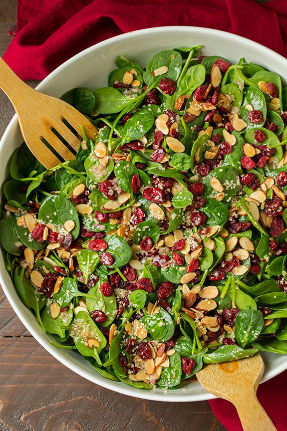 Cranberry Almond Spinach Salad Overhead image of spinach salad in a large salad bowl with wooden serving spoons.