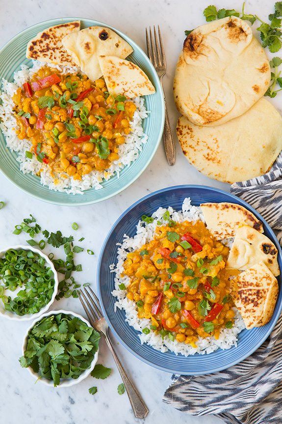 Vegetable Curry Two servings of vegetable curry one in a turquoise bowl and blue bowl. Each is served over basmati rice with a side of naan and garnished with cilantro.