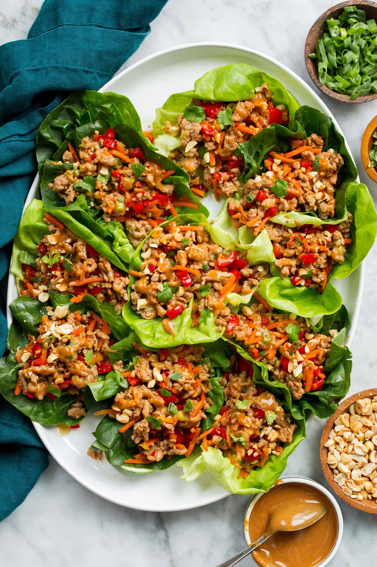 Thai Chicken Lettuce Wraps Thai lettuce wraps shown from above on a white platter on a marble surface with a blue cloth to the side.