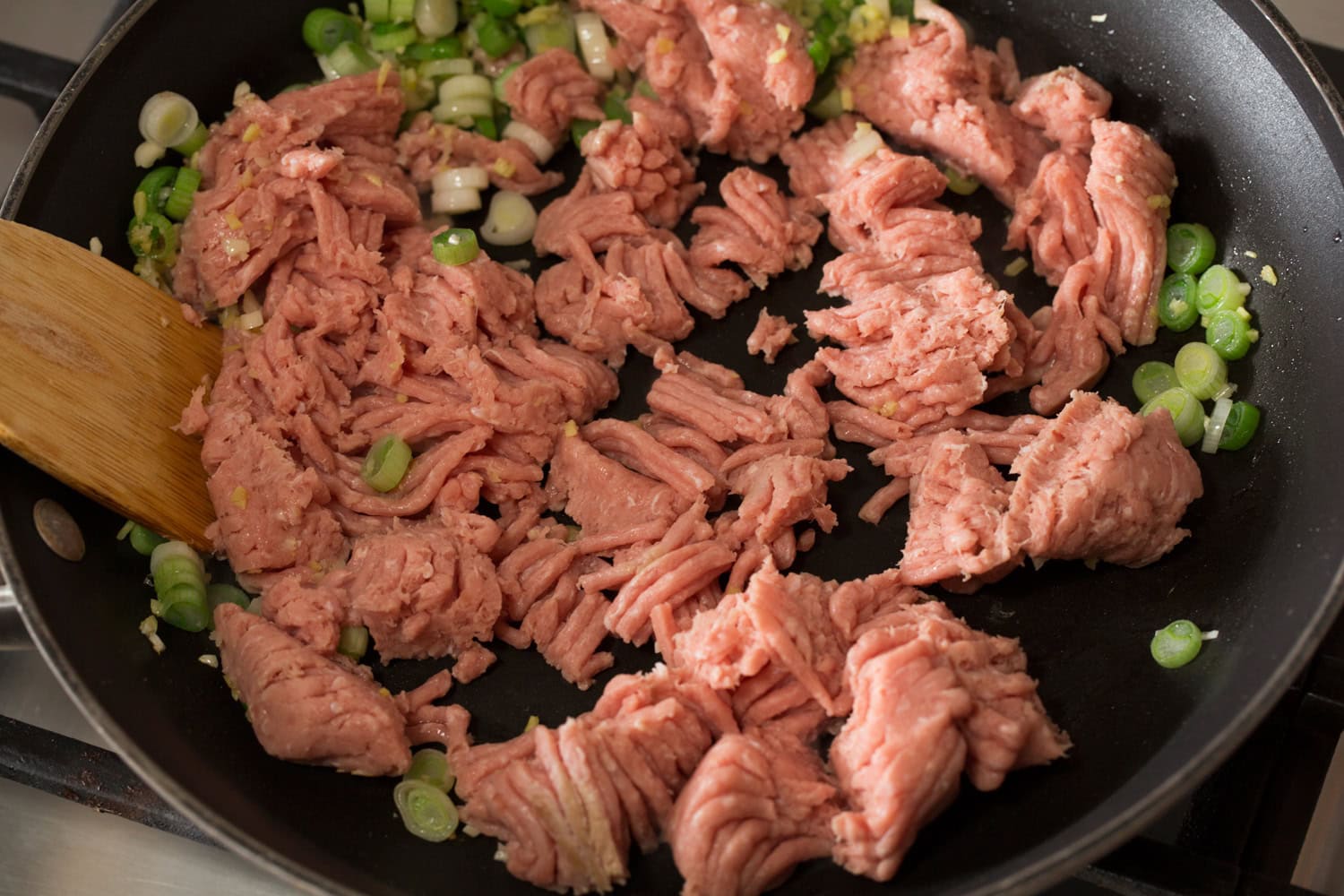 Thai Chicken Lettuce Wraps Ground chicken chunks added to a dark skillet.