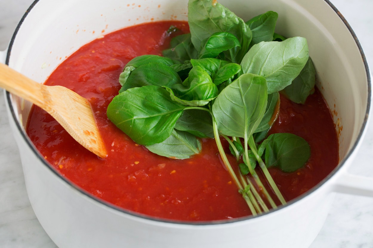 Homemade Marinara Sauce - so much better than the bottled stuff! This is authentic, fresh tasting sauce that you'll want to make again and again! Perfect over just about any type of pasta or served with cheese tortellini. It freezes really well too! #marinara #sauce #recipe #italianfood #dinner #lunch Adding crushed tomatoes and fresh basil to pot.