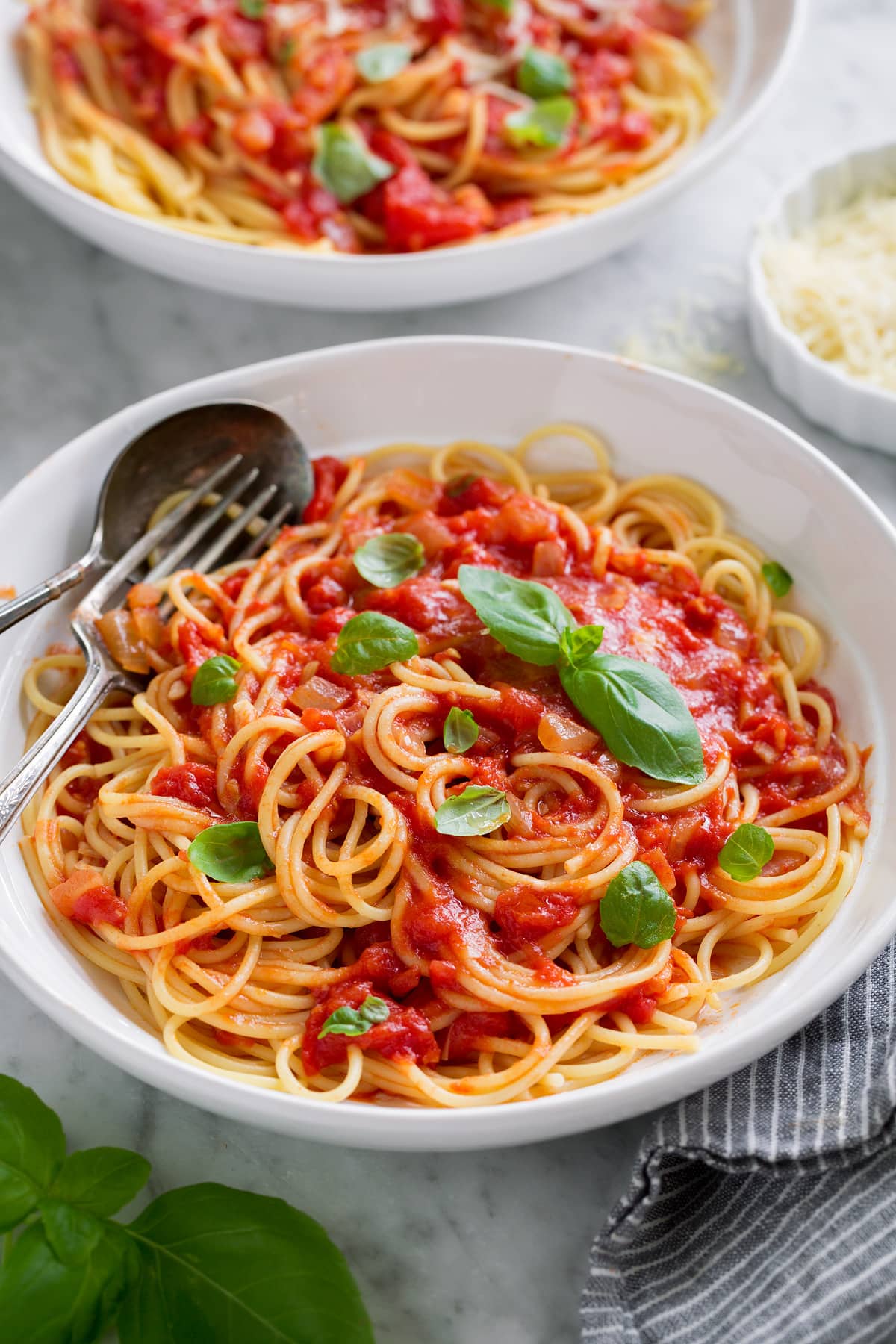 Homemade Marinara Sauce - so much better than the bottled stuff! This is authentic, fresh tasting sauce that you'll want to make again and again! Perfect over just about any type of pasta or served with cheese tortellini. It freezes really well too! #marinara #sauce #recipe #italianfood #dinner #lunch Marinara sauce served tossed with spaghetti, parmesan and fresh basil. Shown in a white pasta bowl.