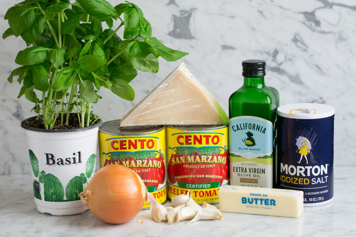 Homemade Marinara Sauce - so much better than the bottled stuff! This is authentic, fresh tasting sauce that you'll want to make again and again! Perfect over just about any type of pasta or served with cheese tortellini. It freezes really well too! #marinara #sauce #recipe #italianfood #dinner #lunch Ingredients needed to make marinara sauce shown here including canned San Marzano tomatoes, extra virgin olive oil, garlic, butter, parmesan, basil, onion, and salt.