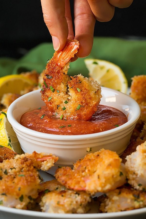 Crispy Panko Crusted Shrimp Cooked shrimp coated with panko being dipped in cocktail sauce in a white small bowl.