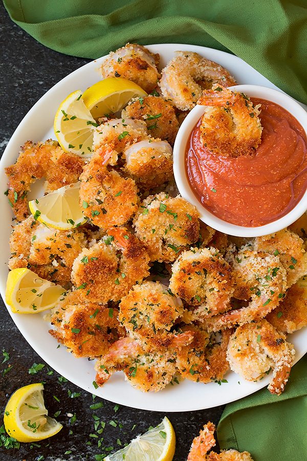Crispy Panko Shrimp Mound of panko shrimp on a serving plate one shrimp is being dipped in cocktail sauce on the side.