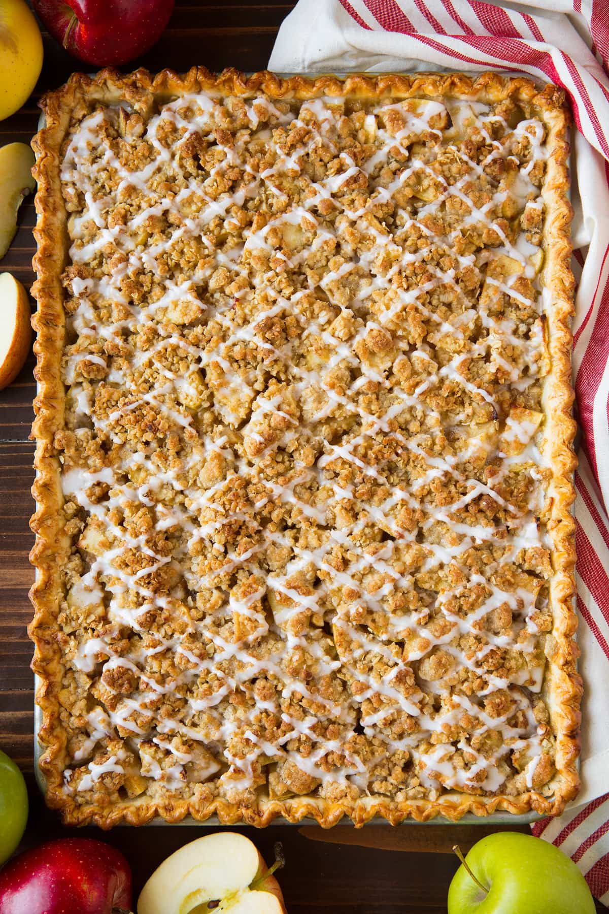 Apple Slab Pie Apple slab pie with crumb topping and icing, after it has finished baking. Pie is in a rimmed sheet pan and set over a dark wooden surface.