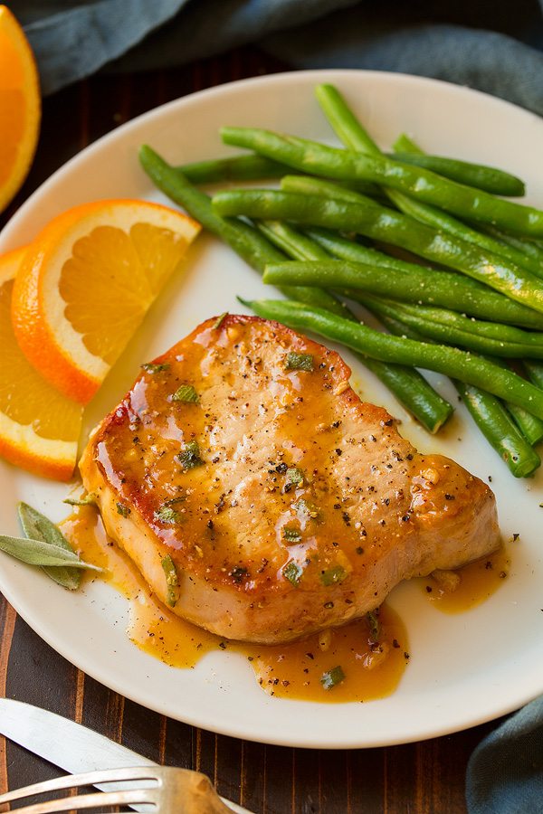 Orange Sage Pork Chops Pork chop on white plate with orange sage sauce. Served with a side of green beans and oranges slices.