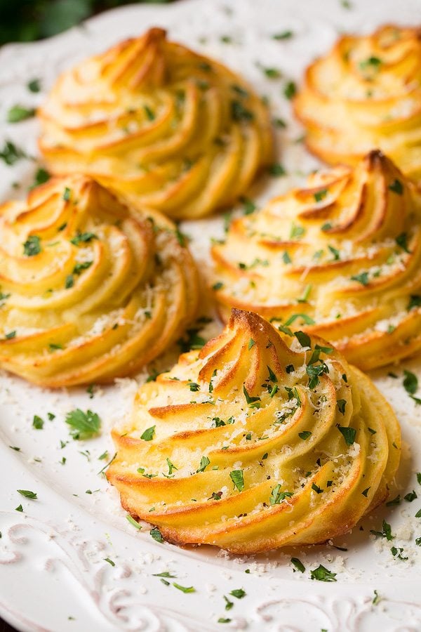 Garlic Parmesan Duchess Potatoes Five Duchess Potatoes shown on a white serving plate, garnished with parsley and parmesan cheese.