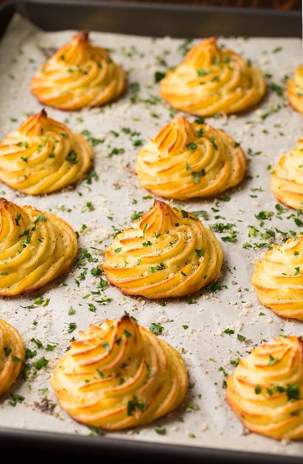 Duchess Potatoes with Garlic and Parmesan Duchess potatoes garnished with parsley and parmesan on a baking sheet.