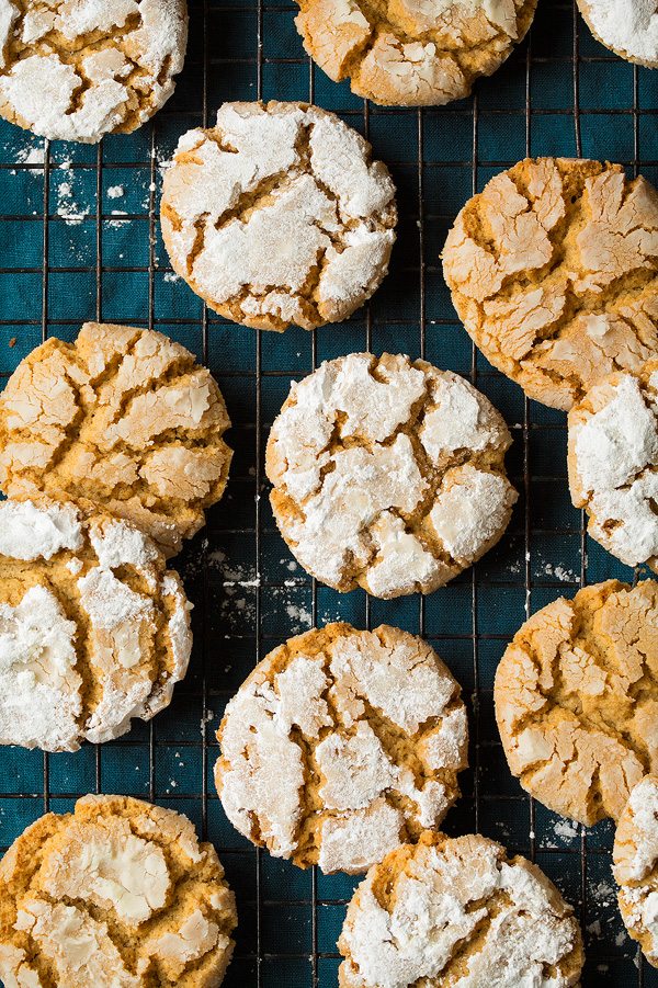 Peanut Butter Crinkle Cookies Peanut Butter Christmas Cookies. Tan peanut butter cookies are covered with powdered sugar and set on a black cooling rack over a blue cloth.
