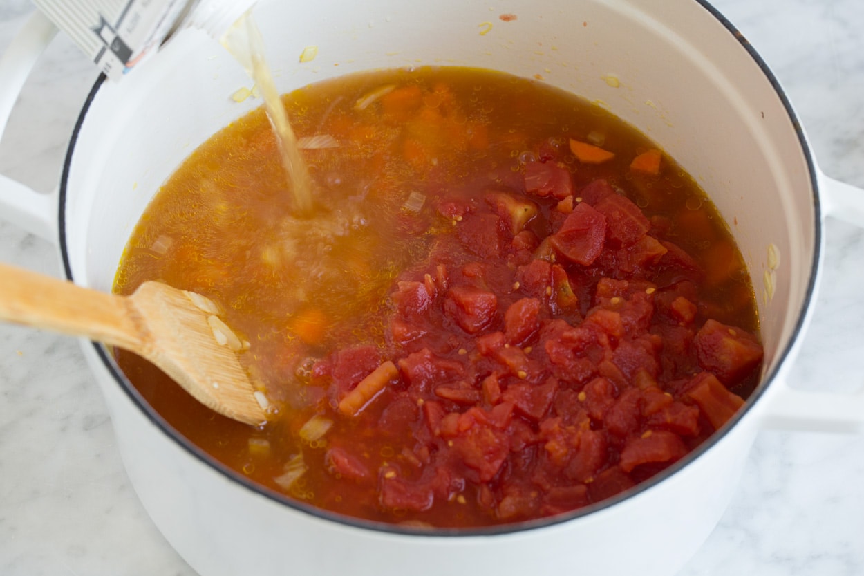 Lentil Soup pouring broth and diced tomatoes into a large pot of lentil soup