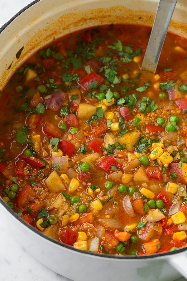 Quinoa Vegetable Stew Quinoa and Vegetable Stew in a large white pot. Ingredients include potatoes, bell peppers, tomatoes, corn, peas, cilantro, broth, quinoa, spices.