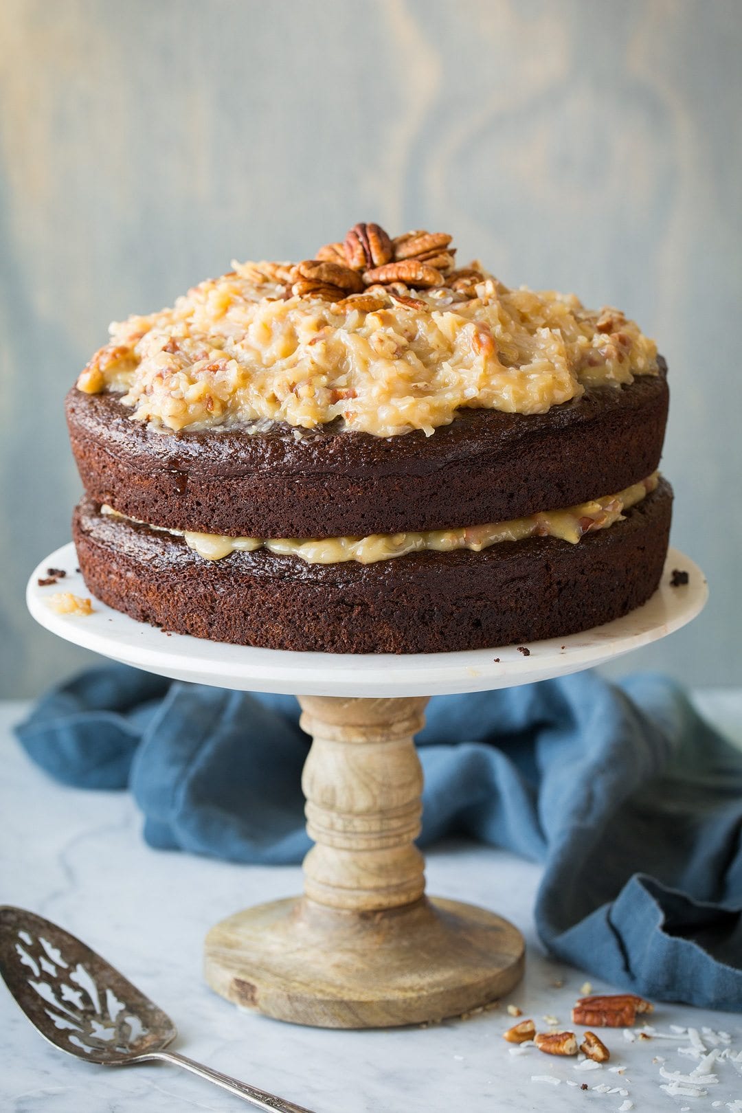 German Chocolate Cake Whole two layer German Chocolate Cake on a marble cake stand with a light blue wooden background.