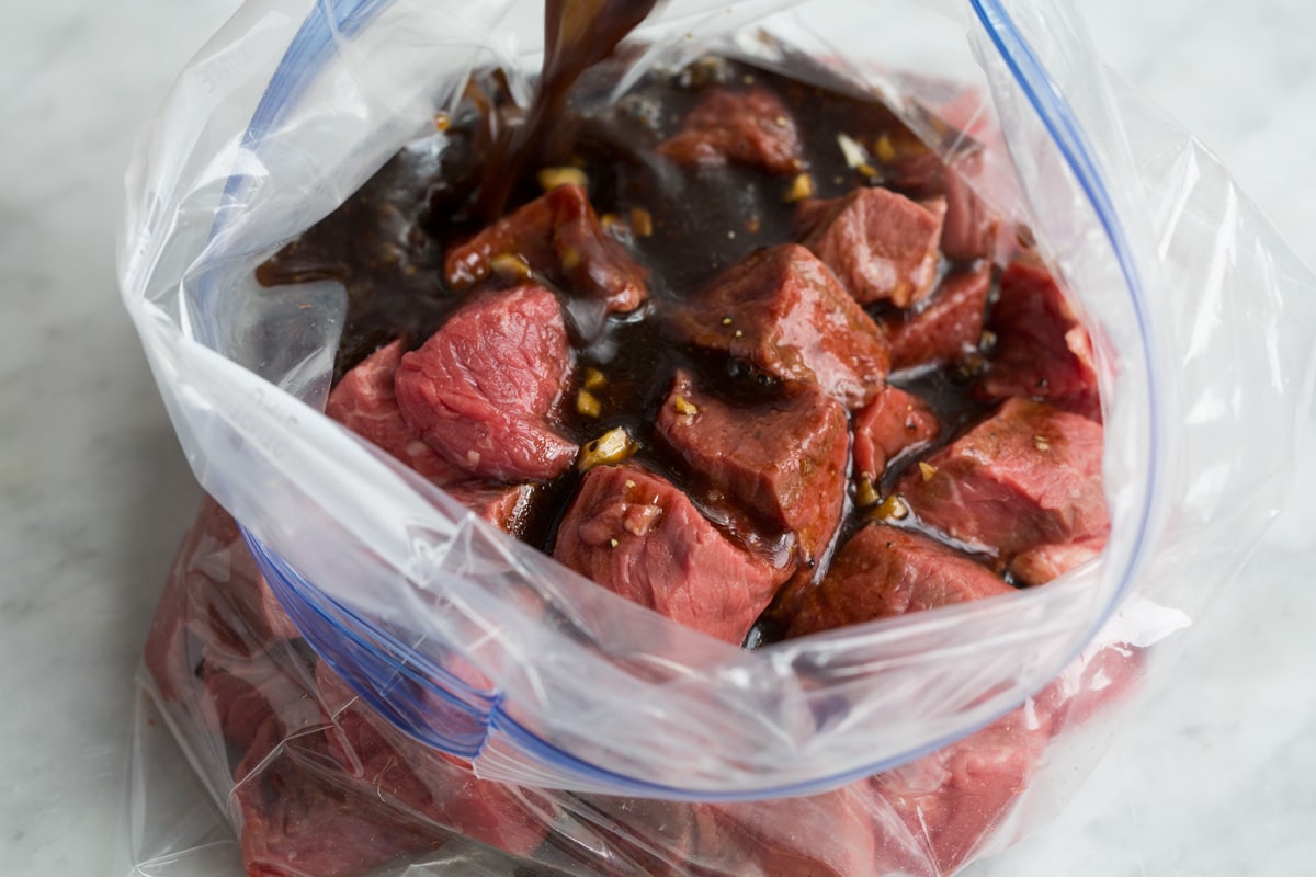 Best Steak Kebabs Pouring marinade over steak cubes in a bag.