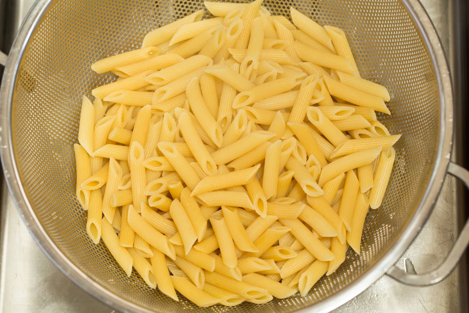 Chicken Caesar Pasta Salad Cooked penne pasta draining in a colander.