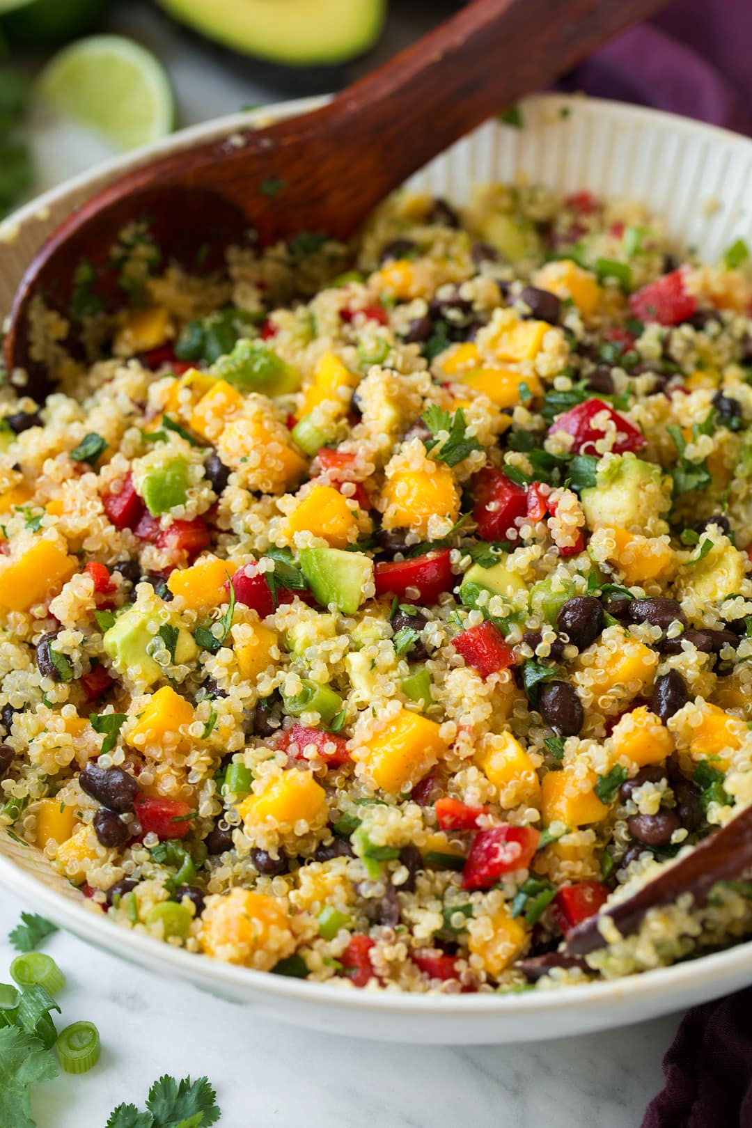 Quinoa salad with mangoes, black beans, avocados and a lime dressing in a large white bowl set over a marble surface.