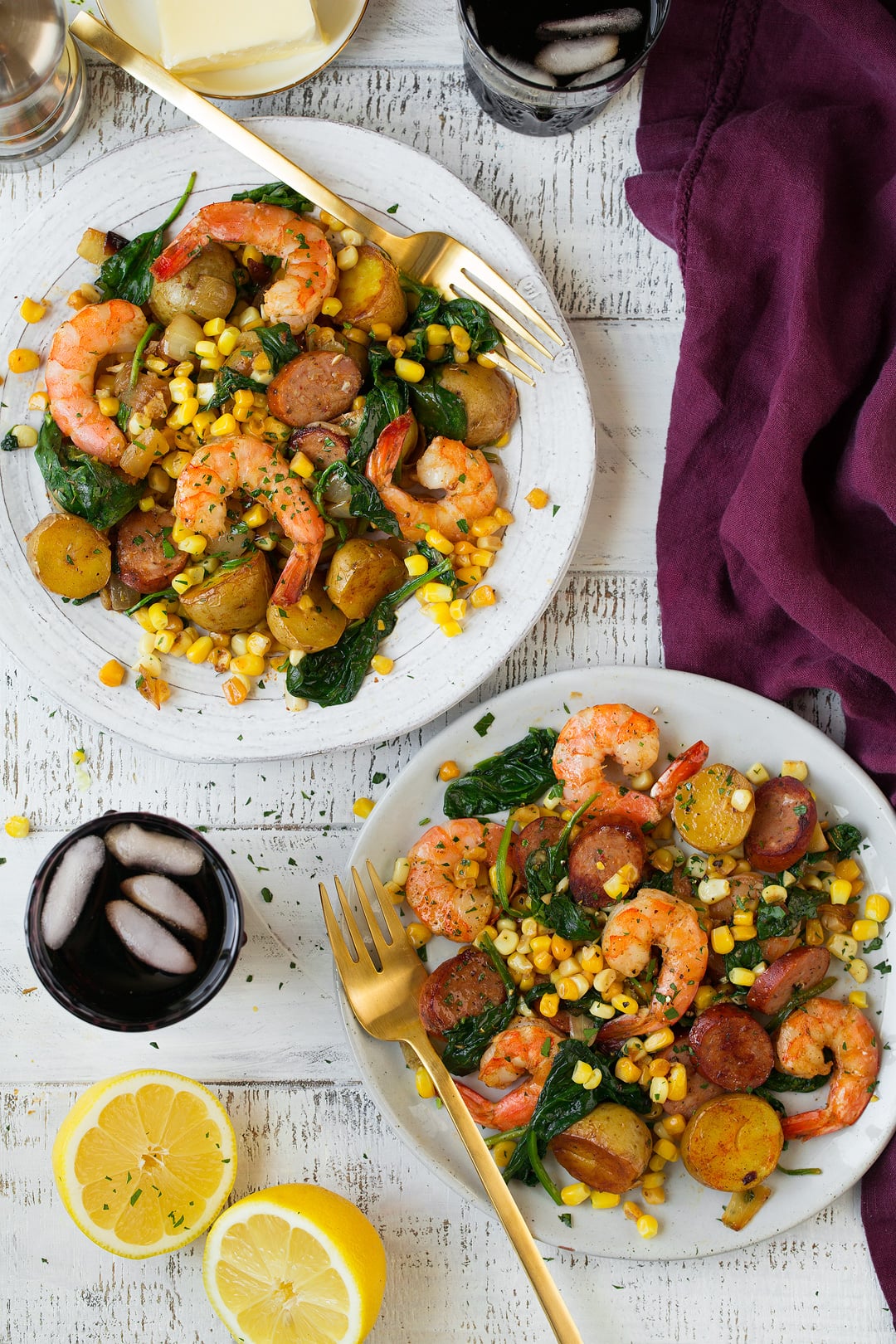 Shrimp Boil Shrimp boil shown here on two white serving plates set over a white wooden background with a maroon napkin and fresh lemons on the side.