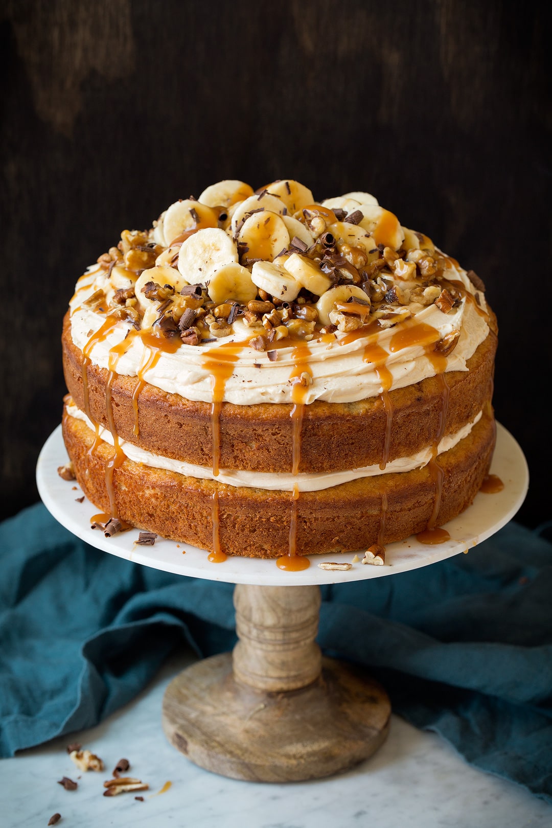 Banana Cake A whole banana cake on a marble and wooden cake stand.