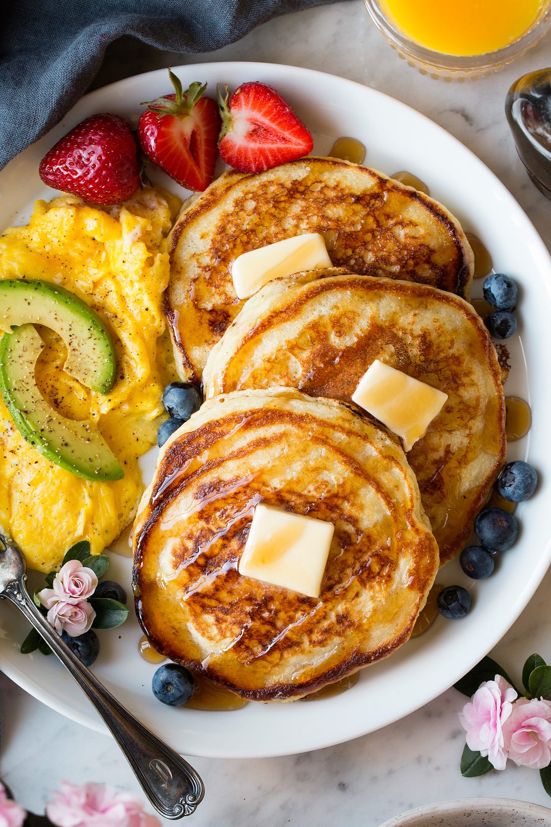 Buttermilk Pancakes Three buttermilk pancakes on a large white blueberries, strawberries and a side of eggs.