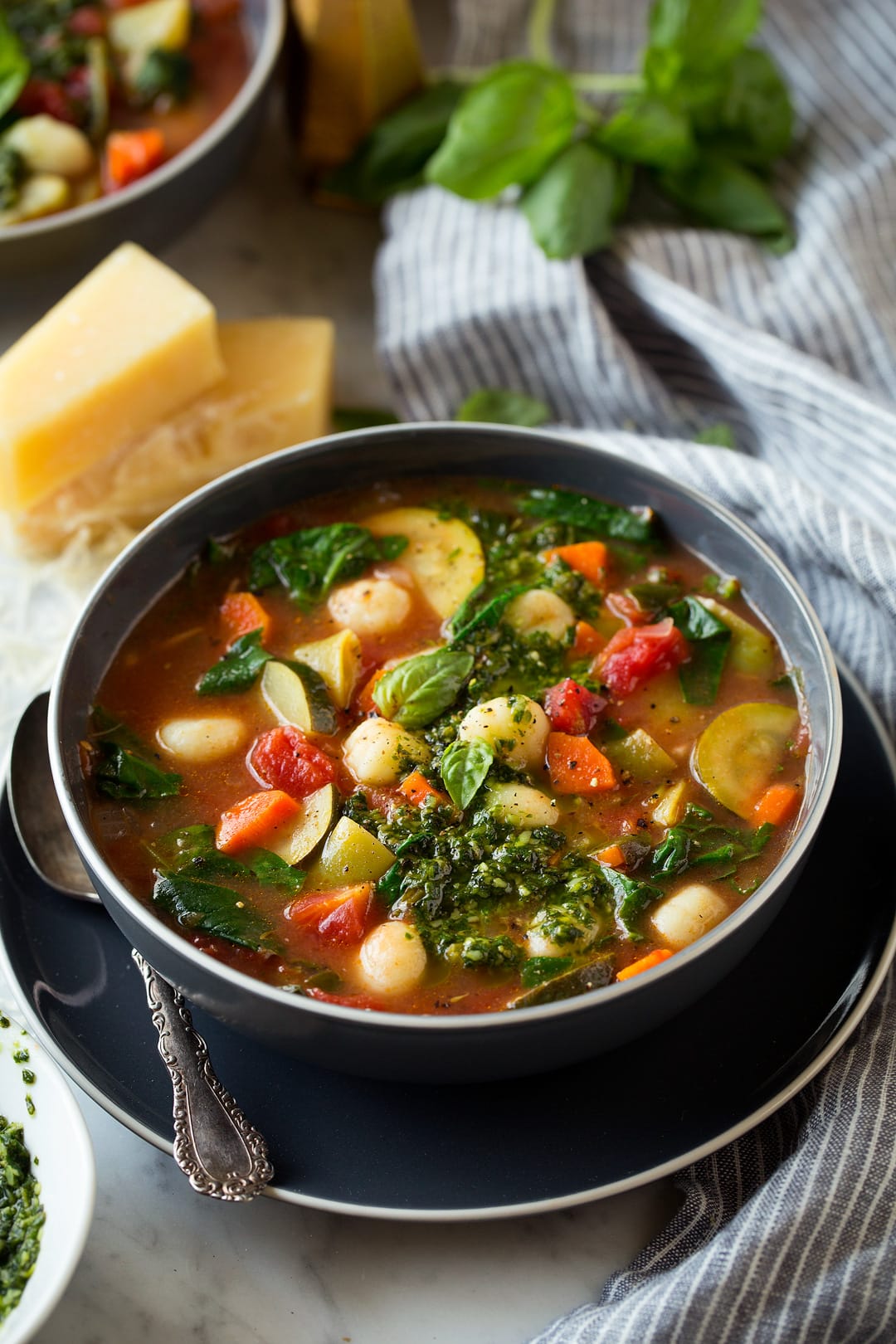 Gnocchi Vegetable Soup with Pesto and Parmesan shown in a single serving in a dark grey bowl