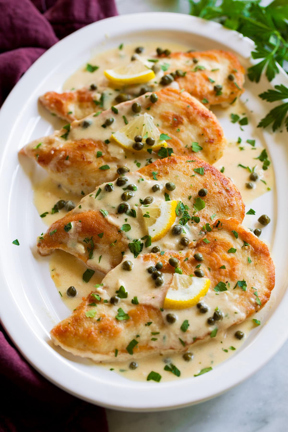 Chicken Piccata 4 servings of chicken piccata on a white oval serving platter.