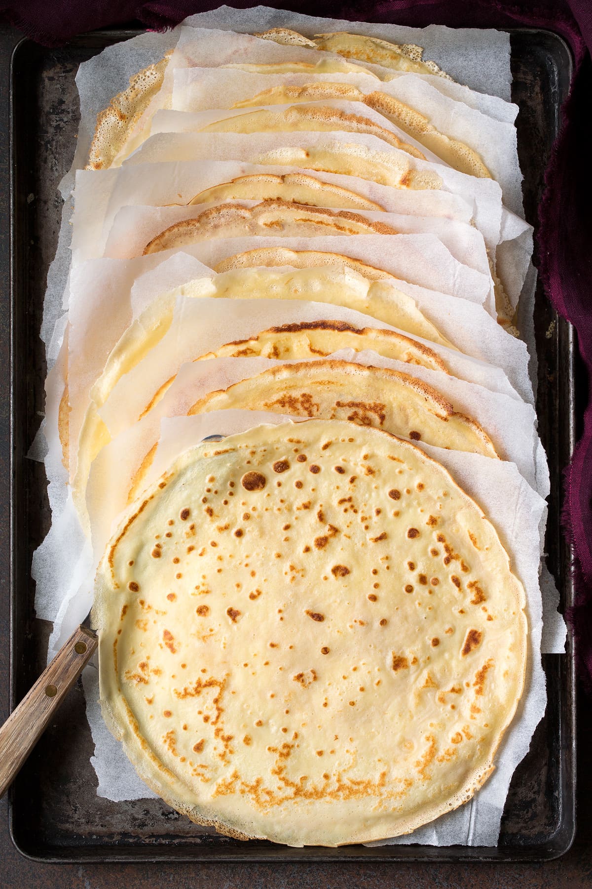 Crepes Recipe Crepes made from scratch, shown after cooking on a baking sheet with parchment paper between each.