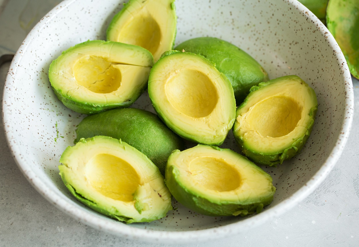 Homemade Guacamole Showing how to make guacamole, adding eight avocado halves to a large white ceramic mixing bowl.