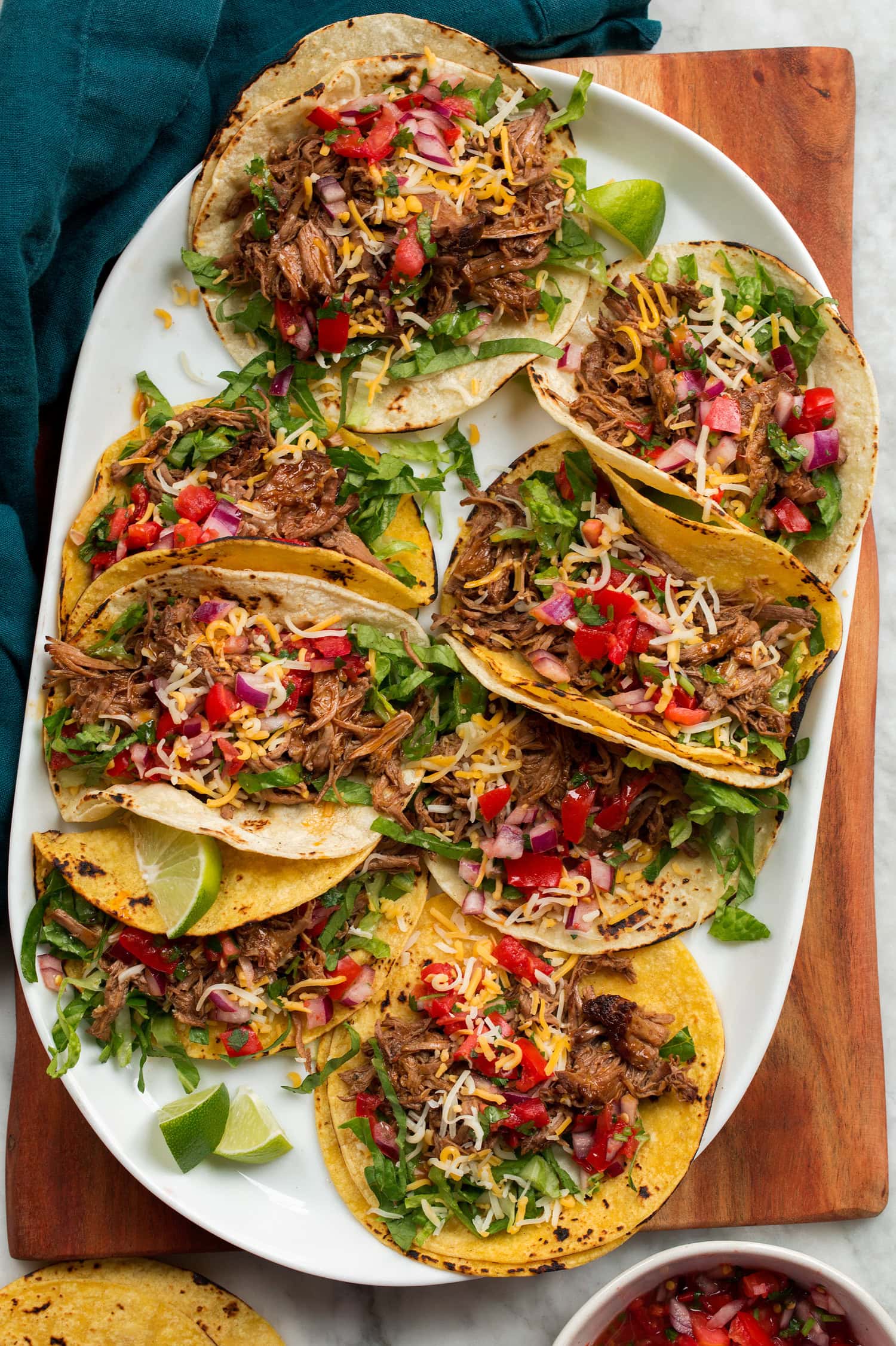 Shredded Beef Tacos Overhead photo of eight shredded beef tacos on a white oval platter set on a wooden tray.