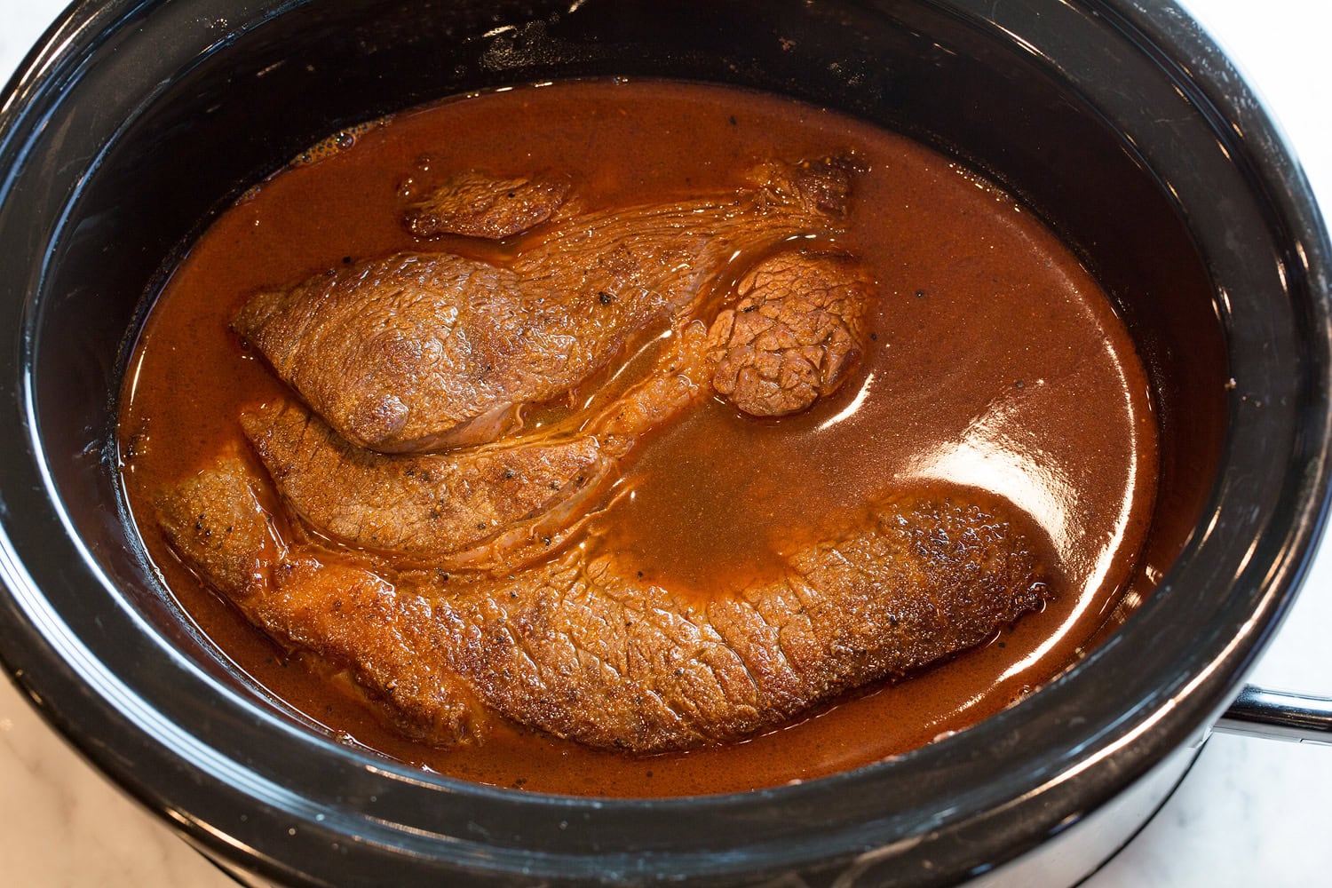 Shredded Beef Tacos Roast covered in chili seasoned broth in slow cooker.