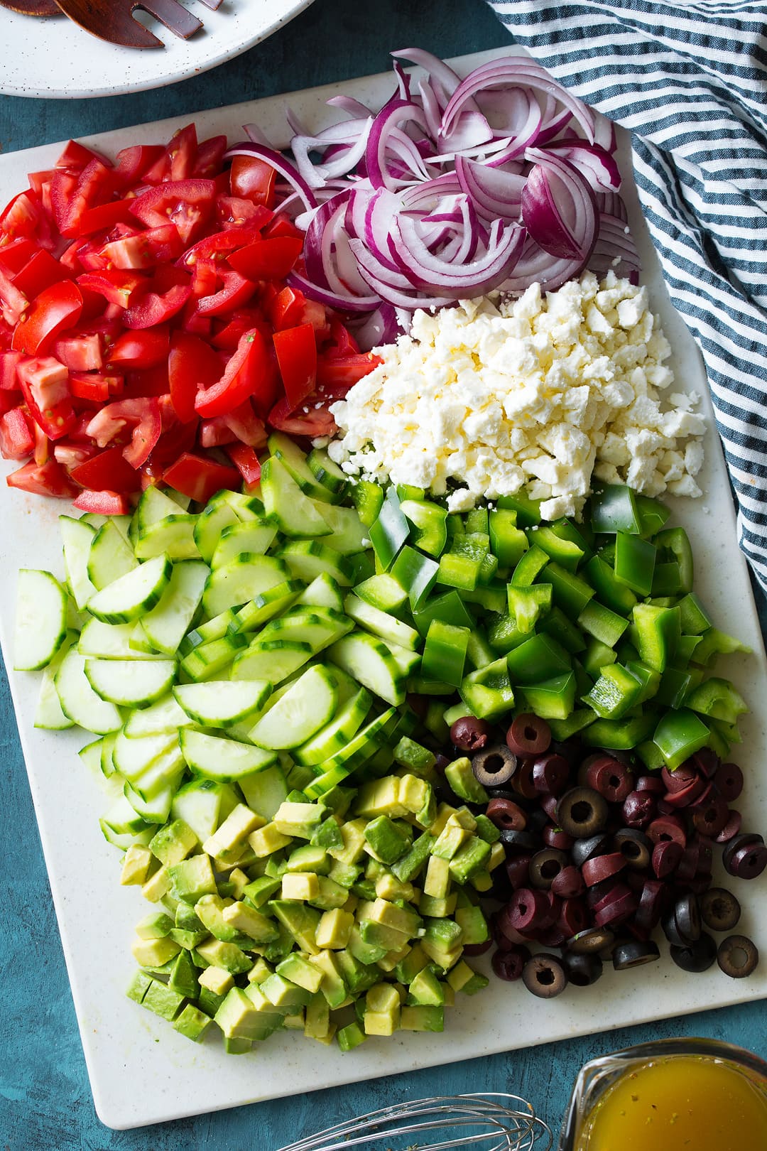 Greek Salad - this is the BEST Greek Salad! So easy to make, it's packed with veggies (love the addition of avocado), and the dressing is so flavorful. A must try recipe! #greek #salad #recipe #vegetables #sidedish #summer Ingredients for making a Greek Salad chopped up on a cutting board