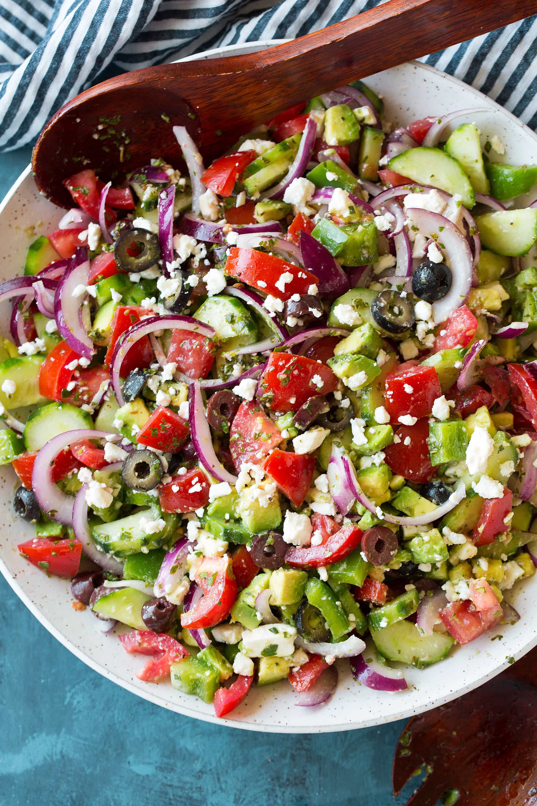 Greek Salad - this is the BEST Greek Salad! So easy to make, it's packed with veggies (love the addition of avocado), and the dressing is so flavorful. A must try recipe! #greek #salad #recipe #vegetables #sidedish #summer An overhead shot of a Greek Salad in a white bowl with salad servers