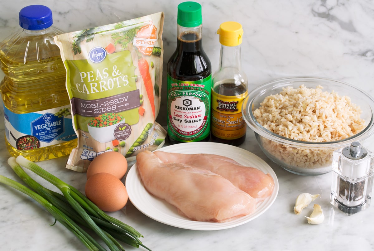 The BEST Chicken Fried Rice Ingredients needed for chicken fried rice shown here including chicken breasts, brown rice, soy sauce, sesame oil, garlic, eggs, green onions, vegetable oil, frozen peas and carrots.