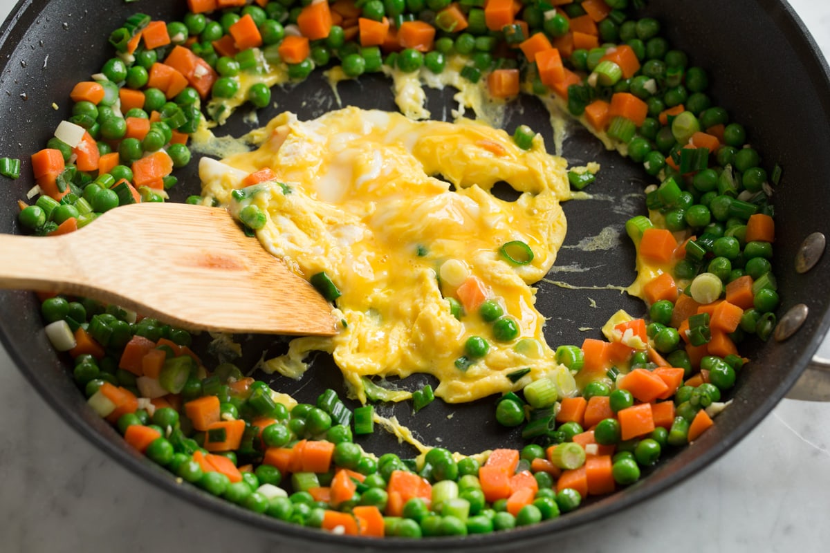 Chicken Fried Rice Scrambling eggs in the center of a ring of vegetables in a skillet for chicken fried rice.